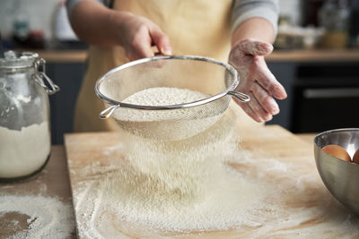 Midsection of woman sifting flour in kitchen