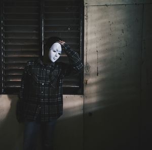 Man wearing mask standing against window