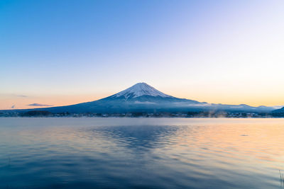 Scenic view of lake by snowcapped mountains against sky during sunset