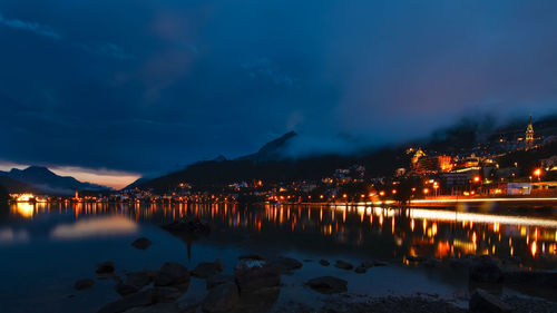 Illuminated city by sea against sky at night