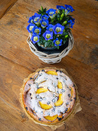 Homemade apricot blueberry cake topped with icing sugar with blue gentian flowers on a wooden table