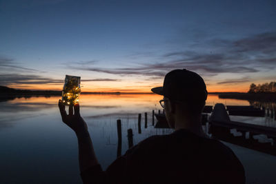 Rear view of silhouette man photographing at sunset