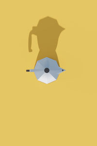 Cropped hand holding umbrella against yellow background