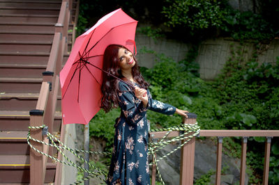 Portrait of woman holding umbrella while standing against railing