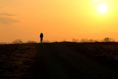 Silhouette man standing on field against sky during sunset