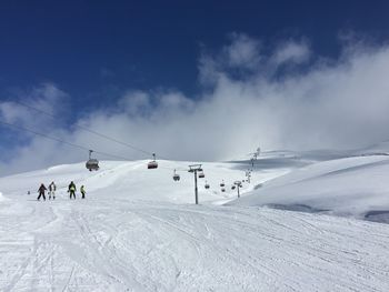 People and cable car over snow covered field against sky