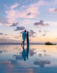 Rear view of man standing at beach against sky during sunset