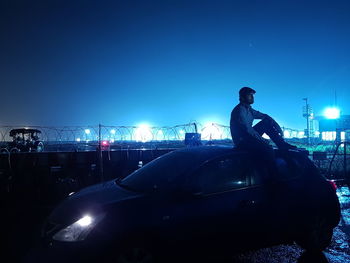 Man standing on illuminated street against clear blue sky at night