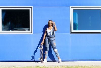 Portrait of young woman standing against blue sky