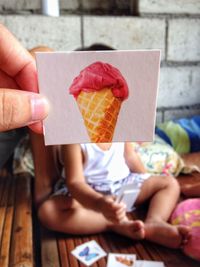 Cropped hand holding ice cream photograph against child