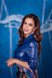 Portrait of young woman standing against blue wall 