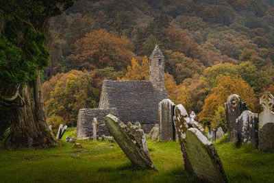 Medieval church and ancient graves in glendalough cemetery with autumn forest and mountains, ireland
