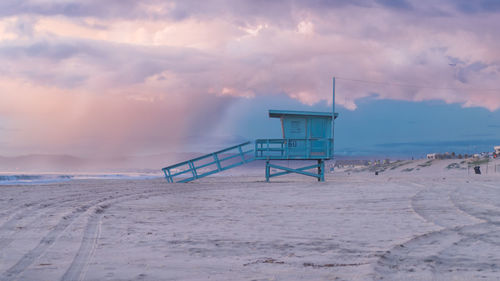 Lifeguard hut on beach against sky during sunset