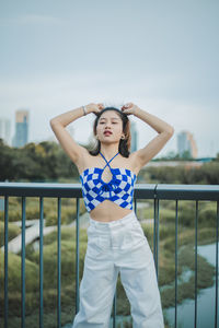 Portrait of young woman standing against railing