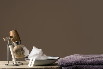 Close-up of shaving equipment and towel on table against colored background