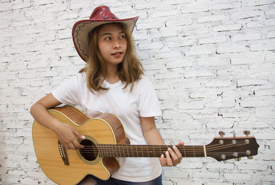 Portrait of a girl playing guitar against wall