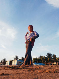 Low angle portrait of young woman standing against sky