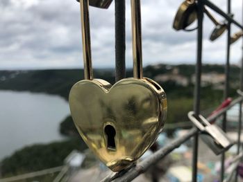 Close-up of heart shape hanging on railing against sky