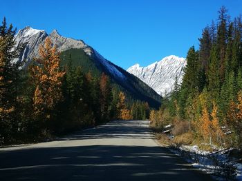 Empty road by snowcapped mountains against clear sky