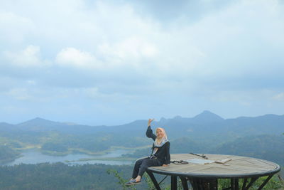 Woman sitting on tower against cloudy sky