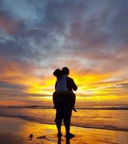 Rear view of people standing at beach during sunset