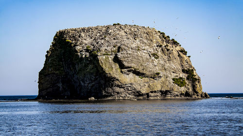 Rock formation in sea against clear sky