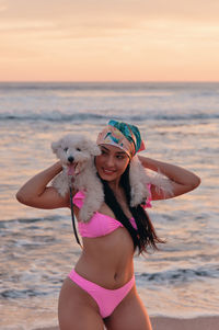 Smiling young woman in bikini with dog at beach