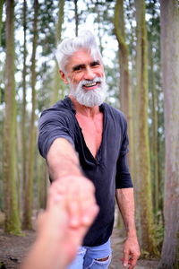 Portrait of smiling mature man holding woman hand at forest