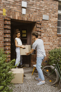 Side view of man passing cardboard box to girlfriend during relocation of house