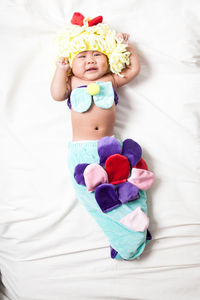 High angle view of baby girl in mermaid costume lying on bed at home