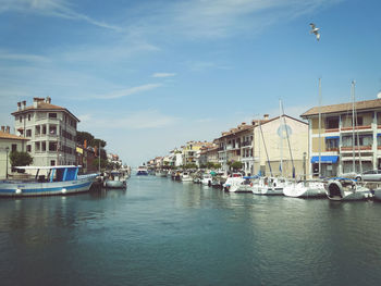 Boats moored on river amidst buildings in city against sky