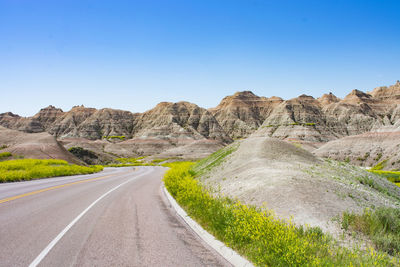 Road leading towards mountains against clear sky