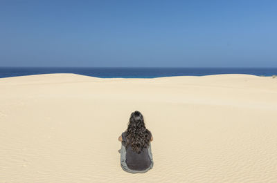 Rear view of person on sand at beach against clear sky