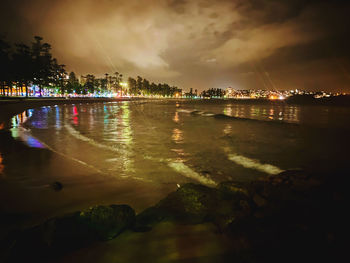 Illuminated city by sea against sky at night