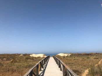 Wooden footbridge on field against clear blue sky