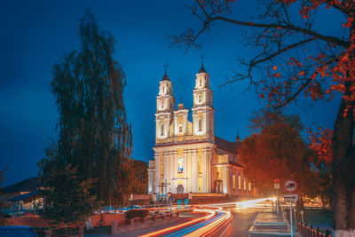 Light trails on road by building against sky at night