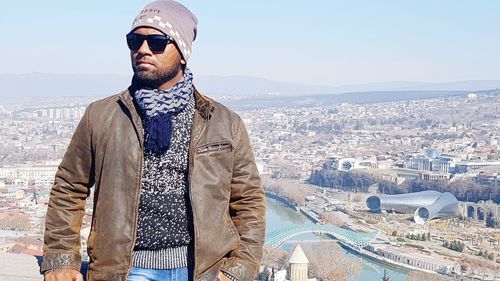 Man in warm clothing against cityscape on sunny day