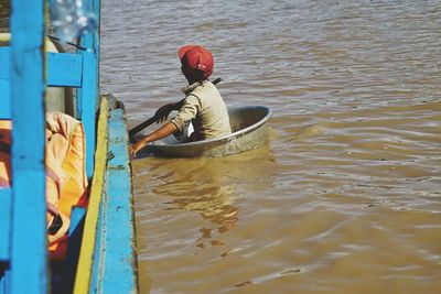 Side view of boy in container by boat on lake