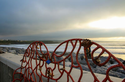 Metallic structure on beach against sky during sunset