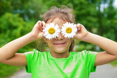 Smiling girl holding flowers in front of eyes