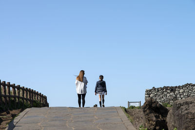 Rear view of mother and daughter walking against clear blue sky