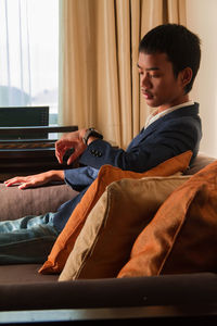 Side view of young man sitting on bed at home