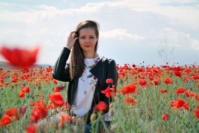 Portrait of woman standing by poppy flowers on field