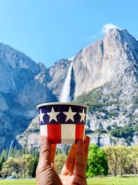 Close-up of hand holding flag against mountain range