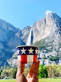 Optical illusion of person holding paper cup against waterfall