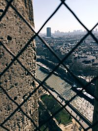 Seine river amidst cityscape against sky seen through chainlink fence