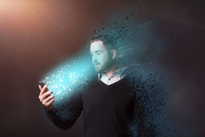 Digital composite image of dissolving man looking at illuminated mobile phone against abstract background