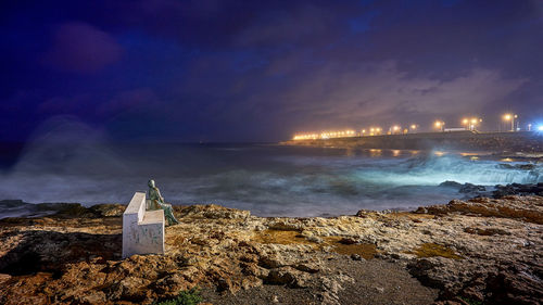 Illuminated buildings by sea against sky