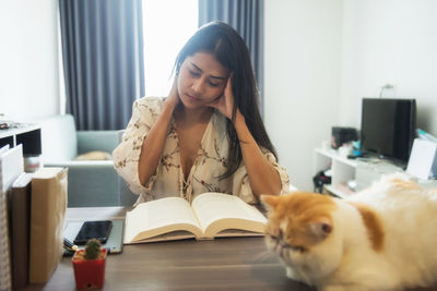 Portrait of young woman with cat sitting on table at home