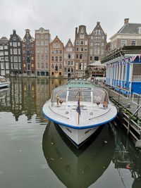 Sailboats moored on canal by buildings against sky